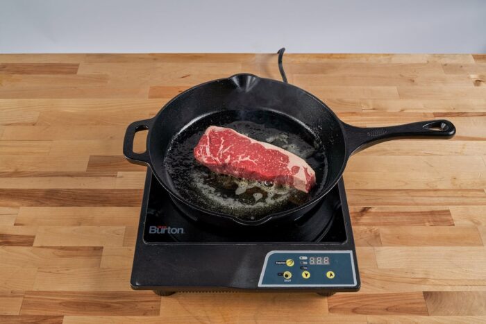 pan frying steak on a stovetop - cooking steak in cast iron pan