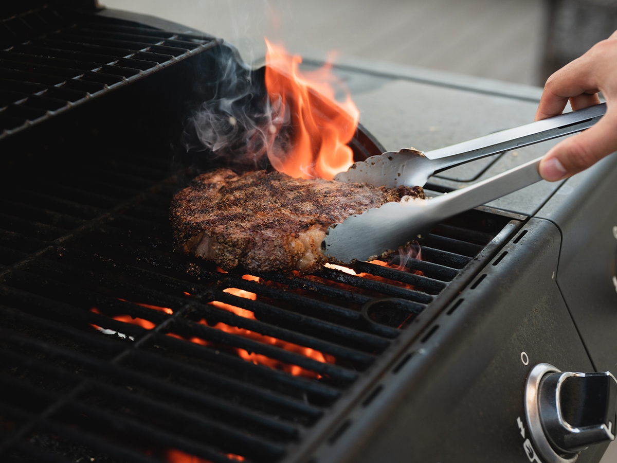 flipping a steak on an open flame grill
